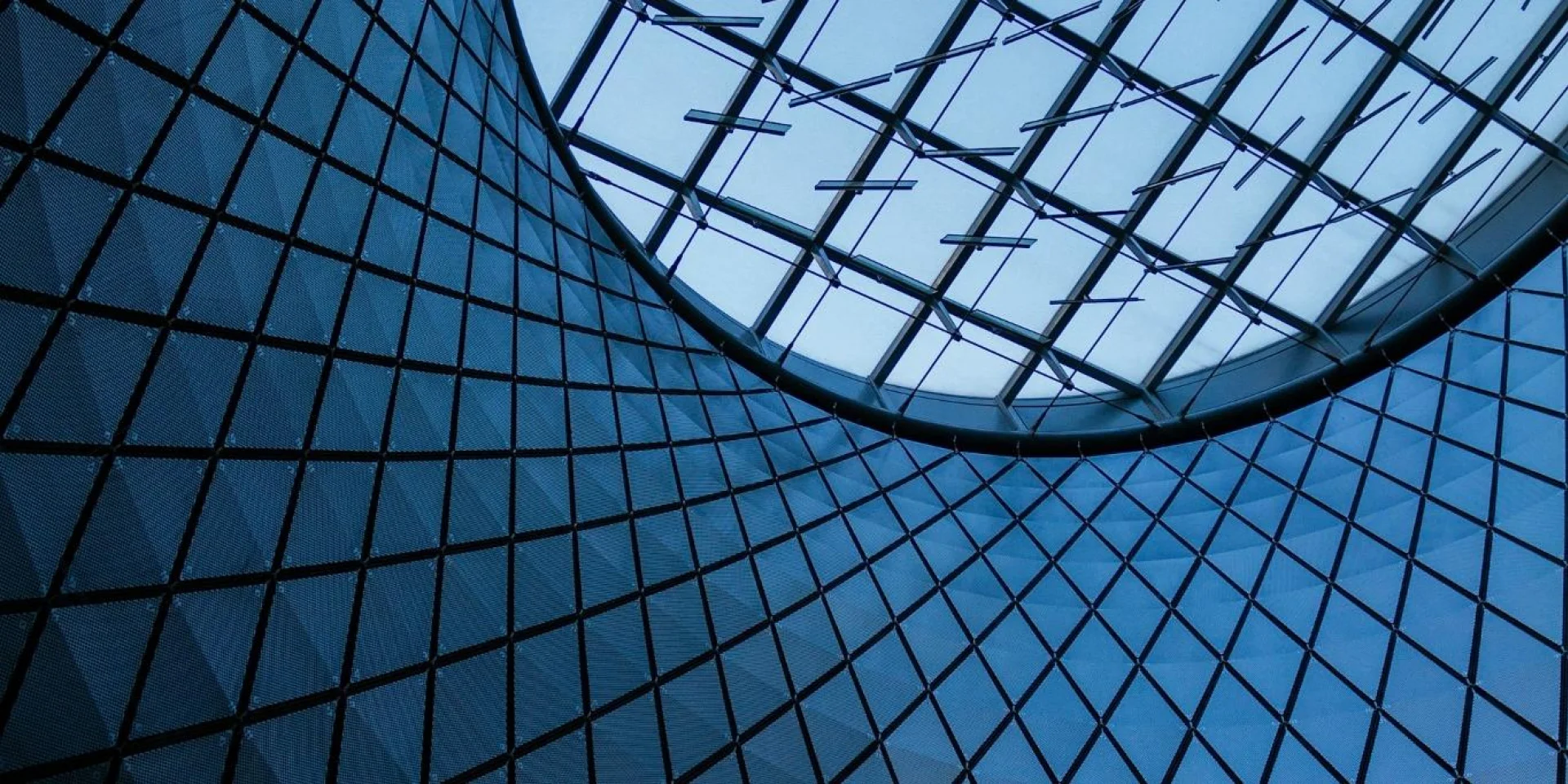 Blue-tinted interior of a building with a circular skylight, featuring a grid-like structure of intersecting lines.