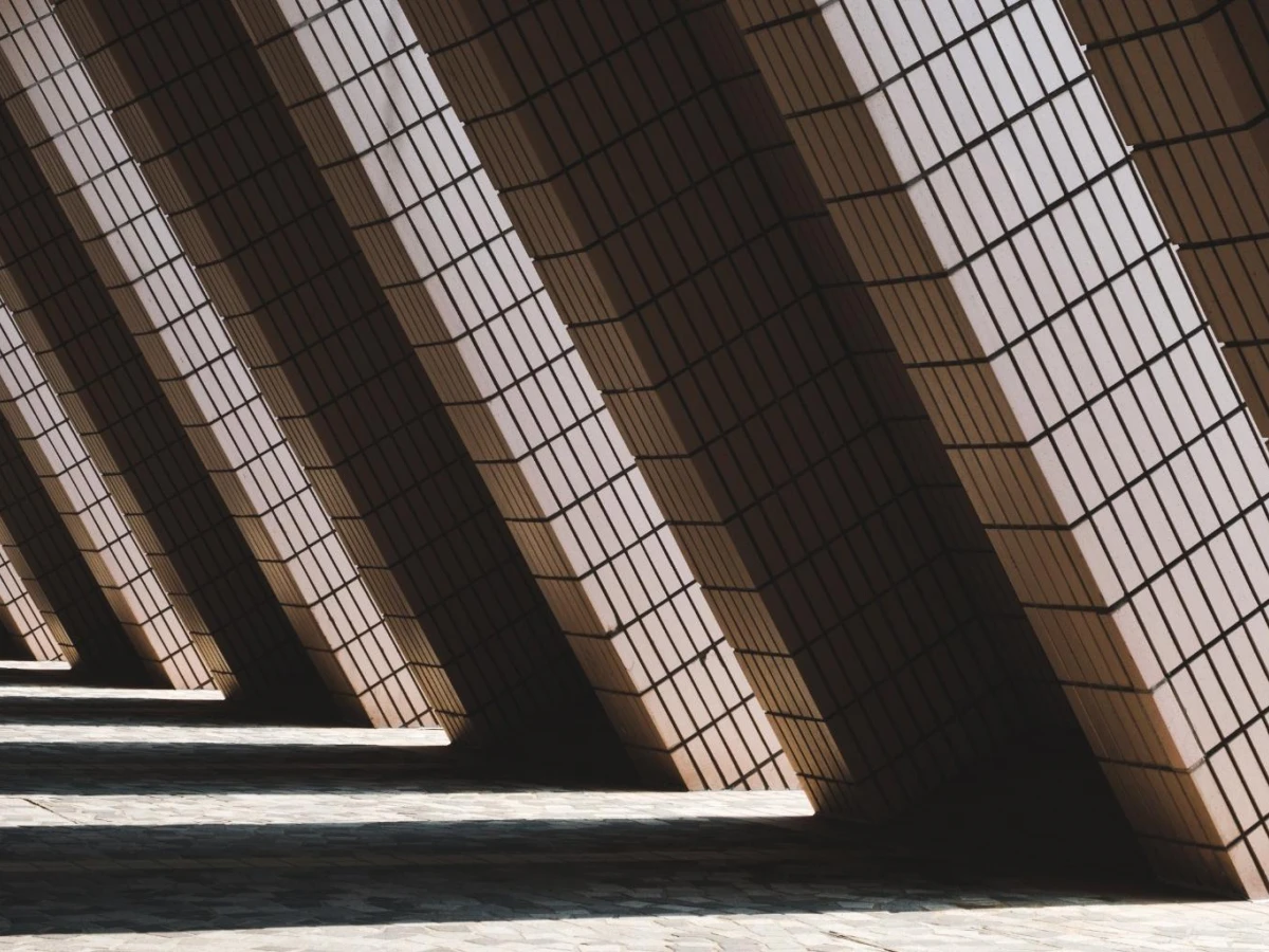 A series of angled columns casting dramatic shadows across a textured floor, creating a geometric pattern with strong contrast between light and dark.